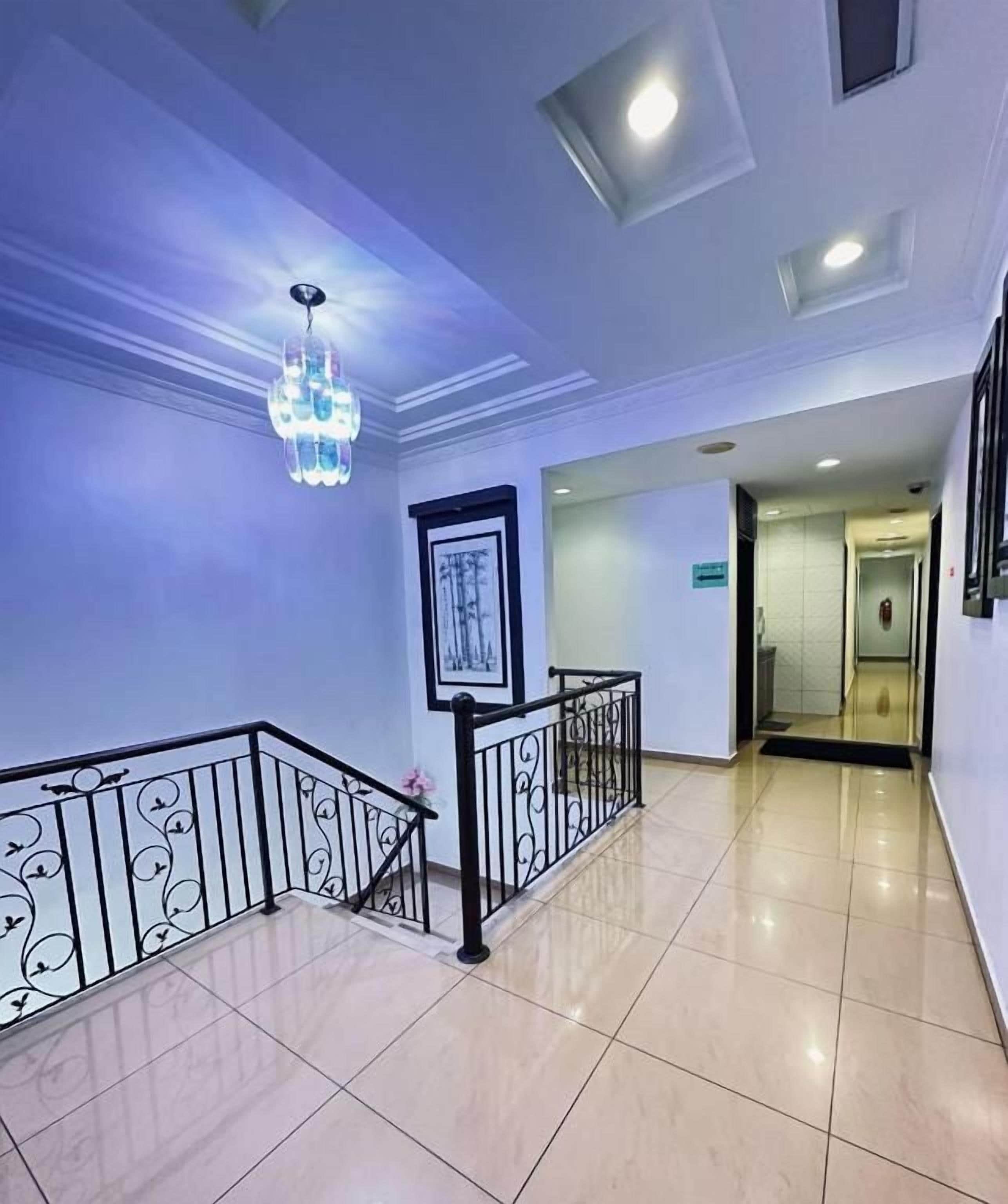 A hotel hallway with a chandelier, framed artwork, and a black railing.