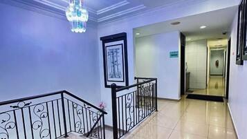 A hotel hallway with a chandelier, framed artwork, and a black railing.