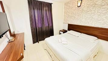 A hotel room with a bed, a wooden desk, a television, and a window with curtains.