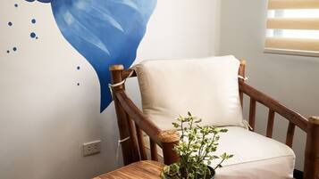Una habitación con una silla de madera, una mesita con una revista, una planta verde y un adorno azul grande en la pared.
