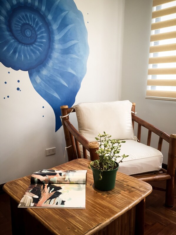 A room with a wooden chair, a small table with a magazine, a green plant, and a large blue wall decoration.