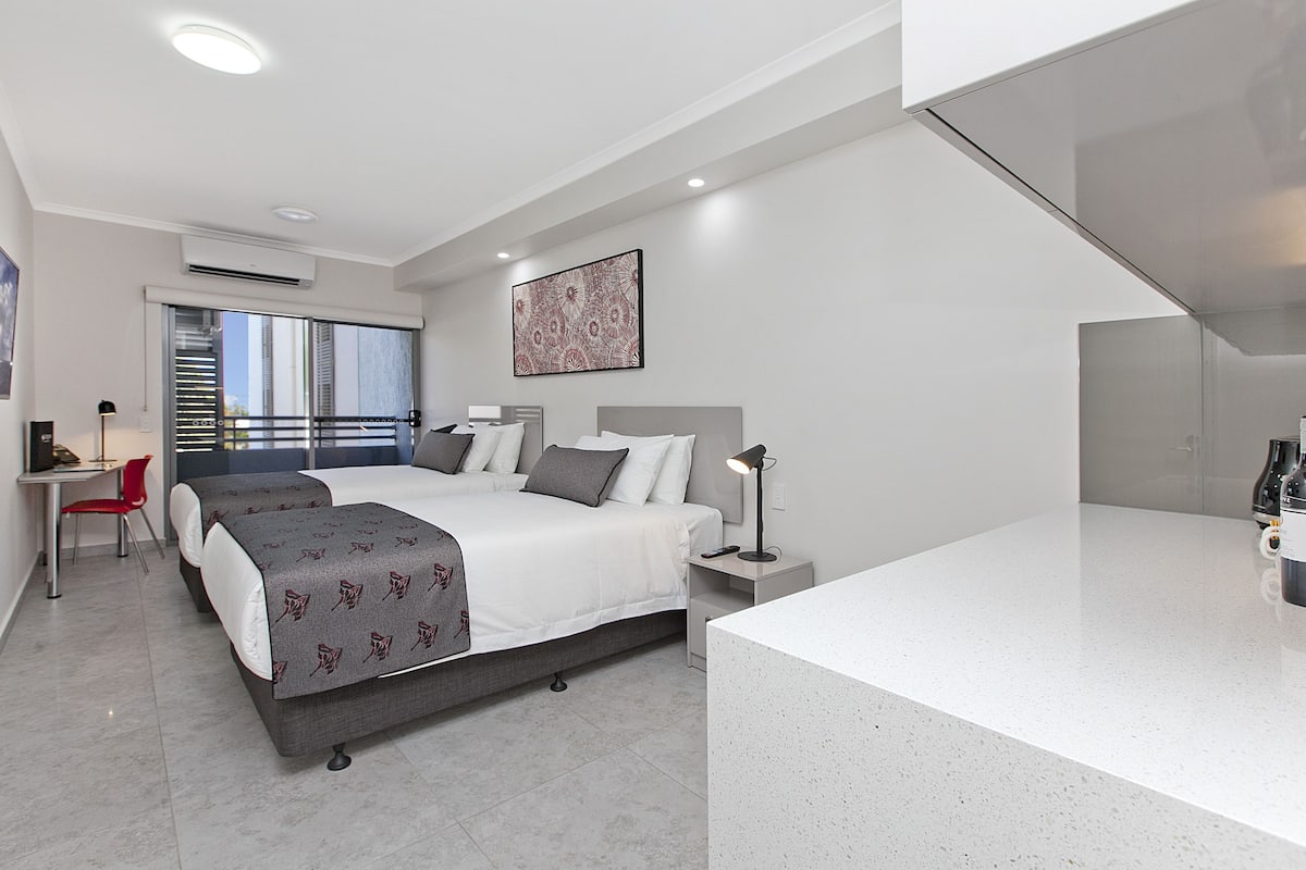 A modern hotel room with two beds, a desk, and a large window with a city view.