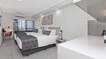 A modern hotel room with two beds, a desk, and a large window with a city view.