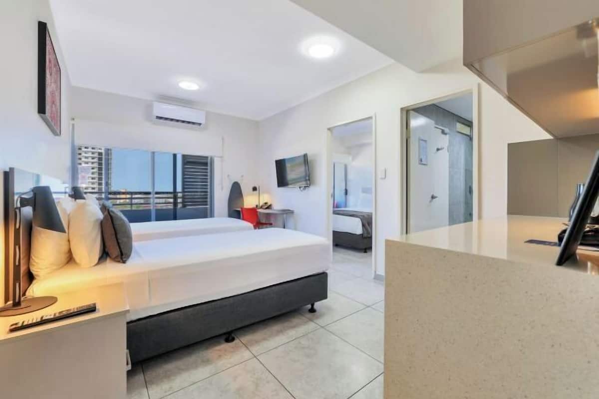 A modern hotel room with a bed, bedside table, lamp, and a TV.