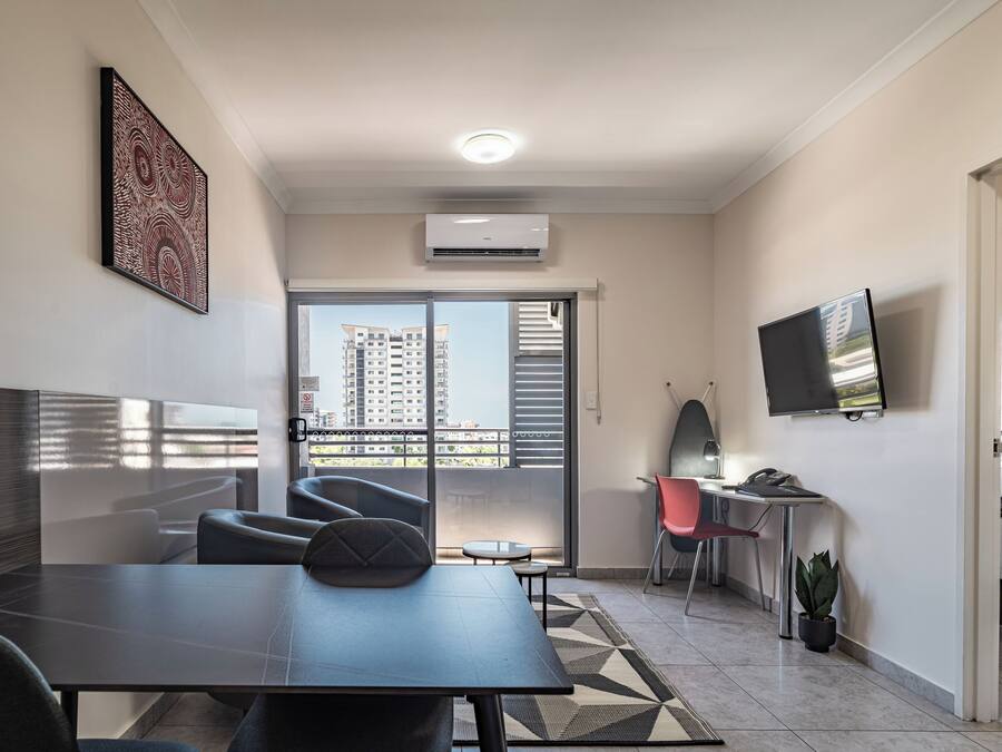 A modern living room with a large window, a flat-screen TV, a dining table, and a sofa.