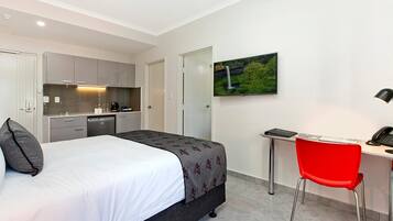 A hotel room with a bed, a desk, a chair, a TV, and a kitchen area.