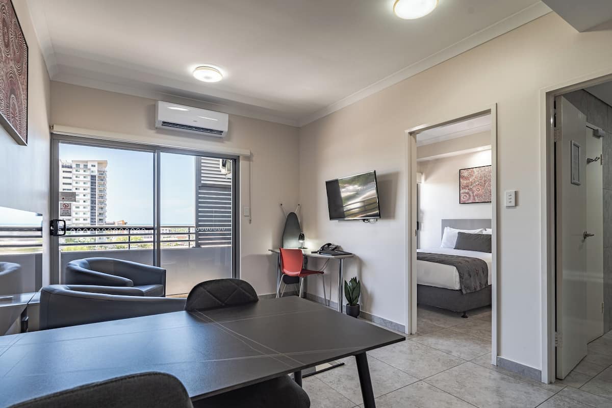 A modern hotel room with a balcony, a dining area, and a bedroom.