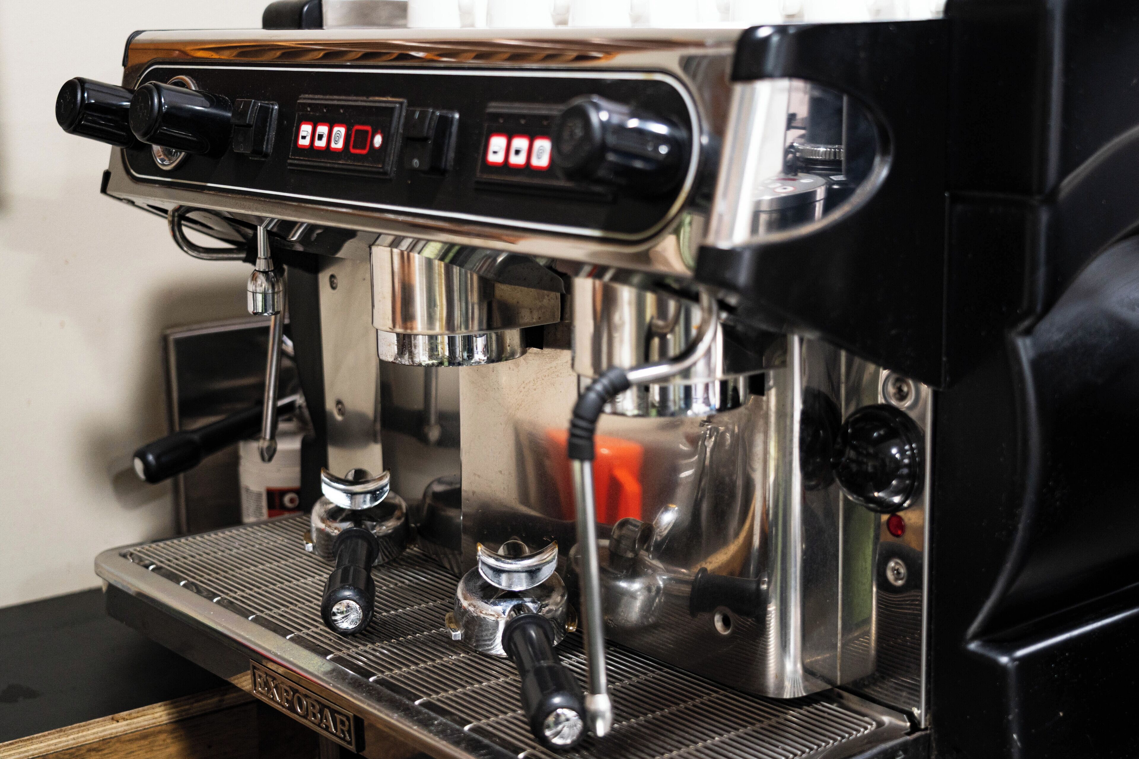A close-up of an espresso machine with a digital display, steam wand, portafilter, and portafilter basket.