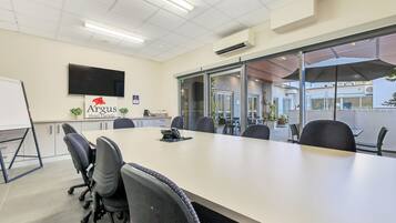 A conference room with a long table, chairs, a whiteboard, and a TV mounted on the wall.