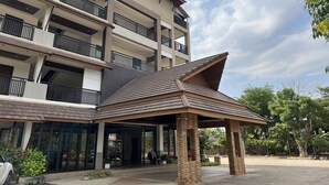 Un hotel de varios pisos con balcones, un espacio exterior cubierto y un estacionamiento.
