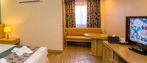 A hotel room with a bed, a sofa, a small table, a television, and an air conditioning unit.
