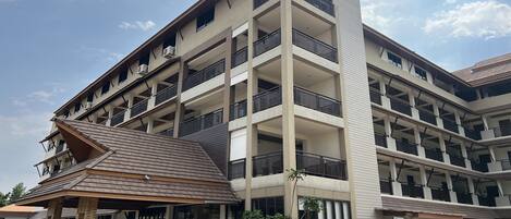 Un hotel de varios pisos con balcones, una entrada cubierta y un estacionamiento.
