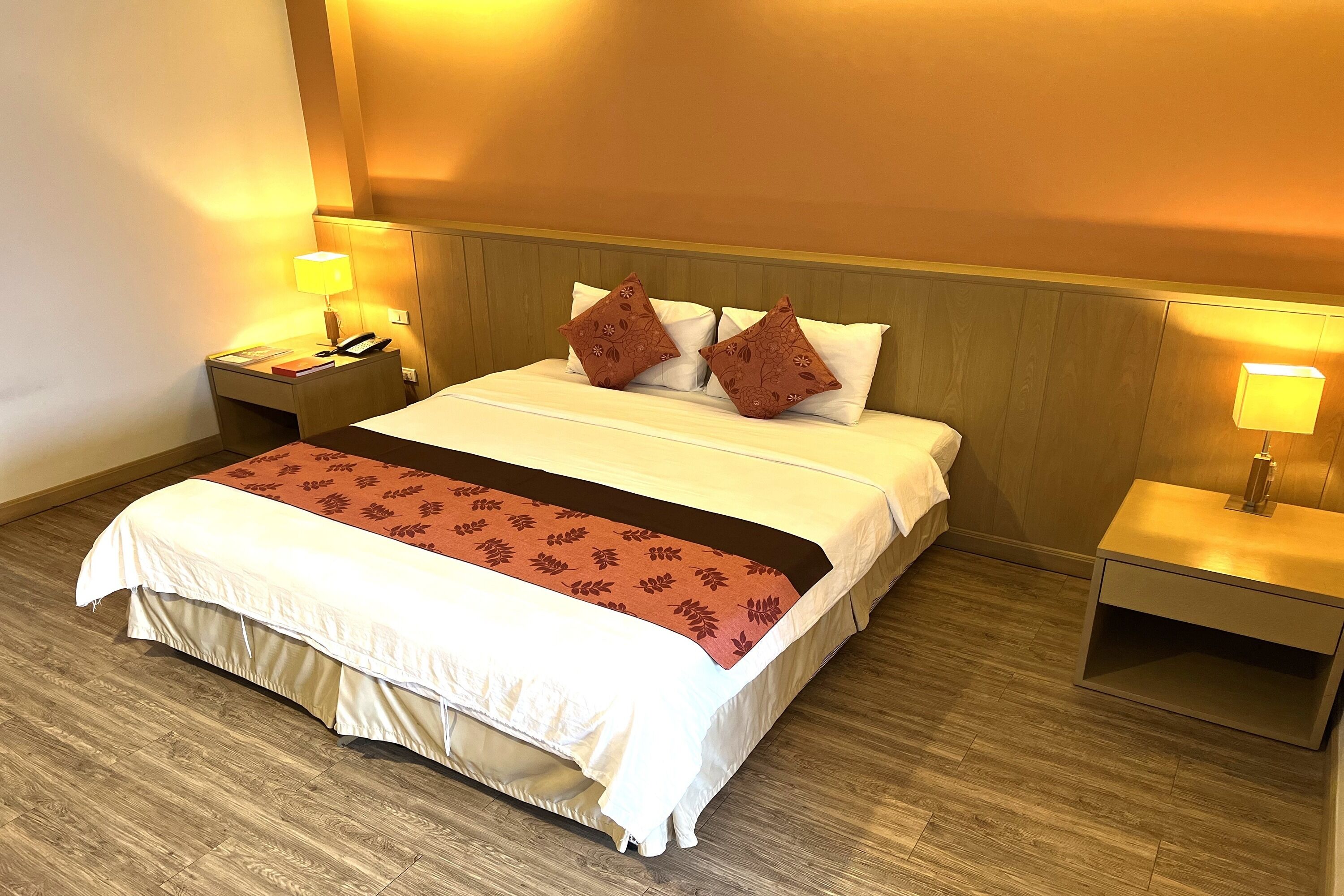 A neatly made bed with a white and red bedspread, two decorative pillows, and a bedside table with a lamp.