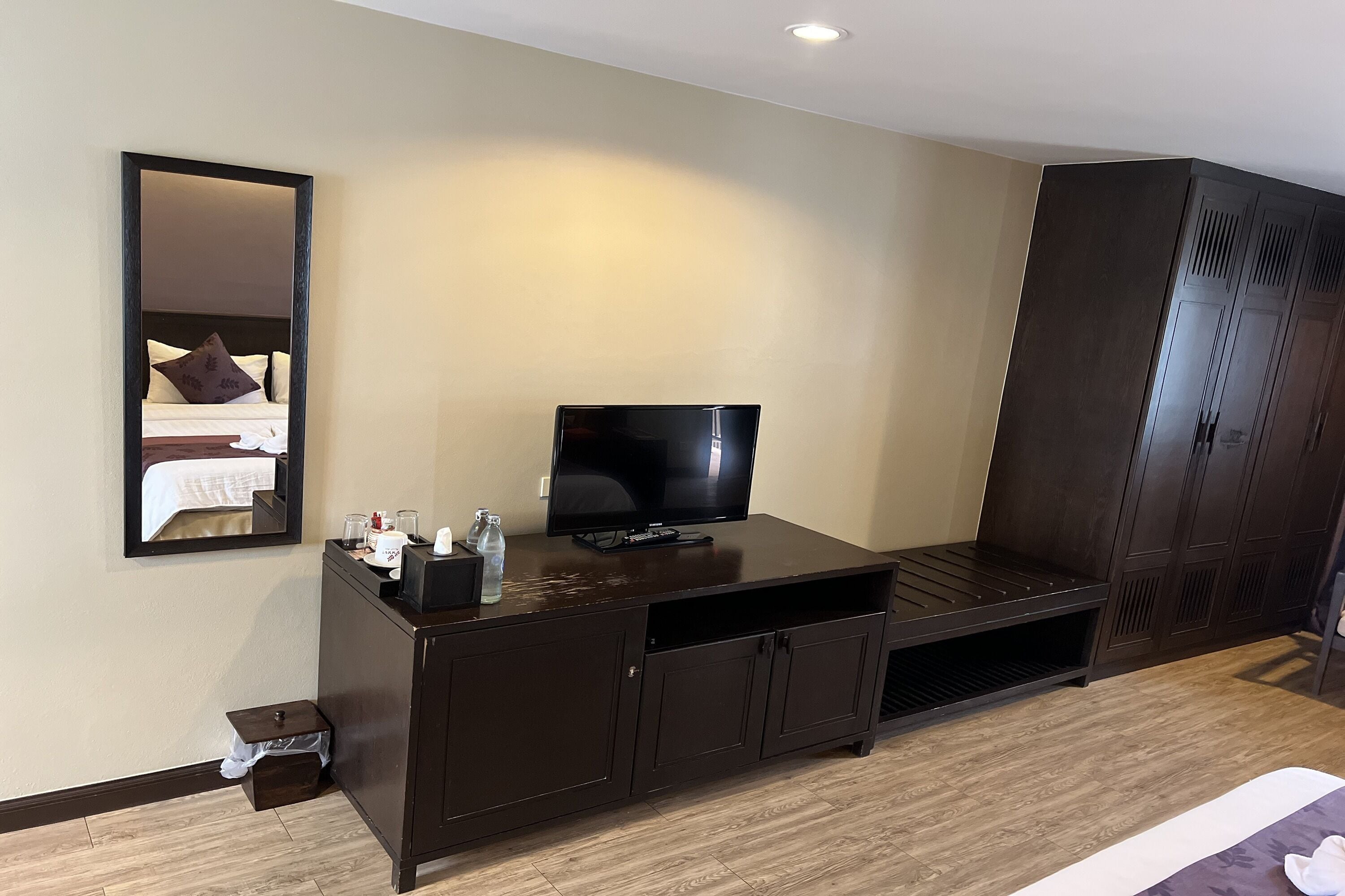 A hotel room with a dark wooden TV stand, a flat-screen TV, a mirror, and a wardrobe.