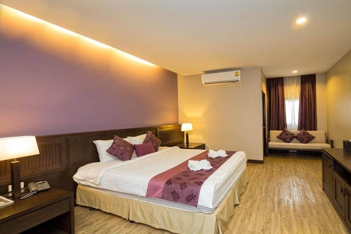 Quarto de hotel com cama, mesa de cabeceira, luminária, ar condicionado e um sofá.