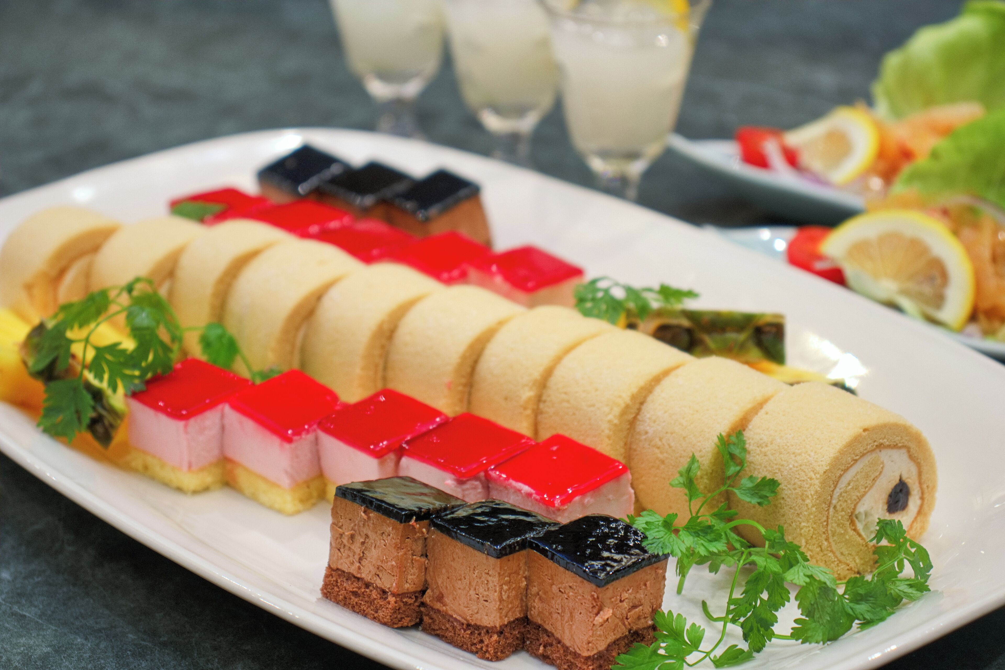 Un plateau de desserts comprenant divers types de sucreries et un rouleau de pâte feuilletée, le tout décoré de persil.