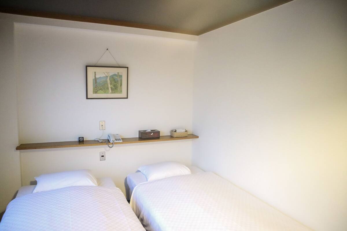 Een kamer met twee éénpersoonsbedden, een houten plank met een telefoon, een stopcontact en een lijst aan de muur.