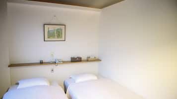 A room with two single beds, a wooden shelf with a telephone, a power outlet, and a framed picture on the wall.