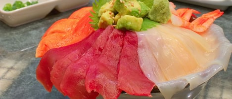 A bowl of sashimi with various types of fish and avocado garnish.