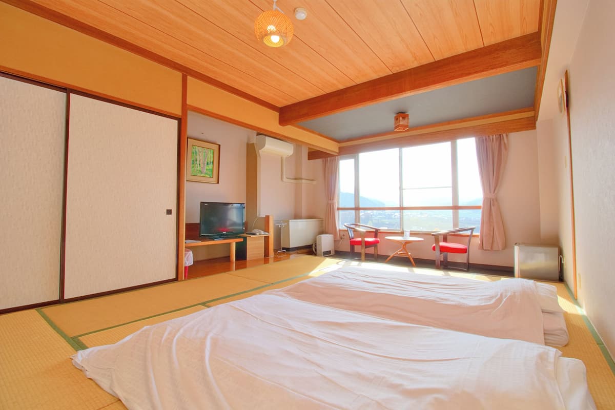 Een traditionele Japanse kamer met tatami vloeren, een groot bed, een televisie en uitzicht op de omgeving.