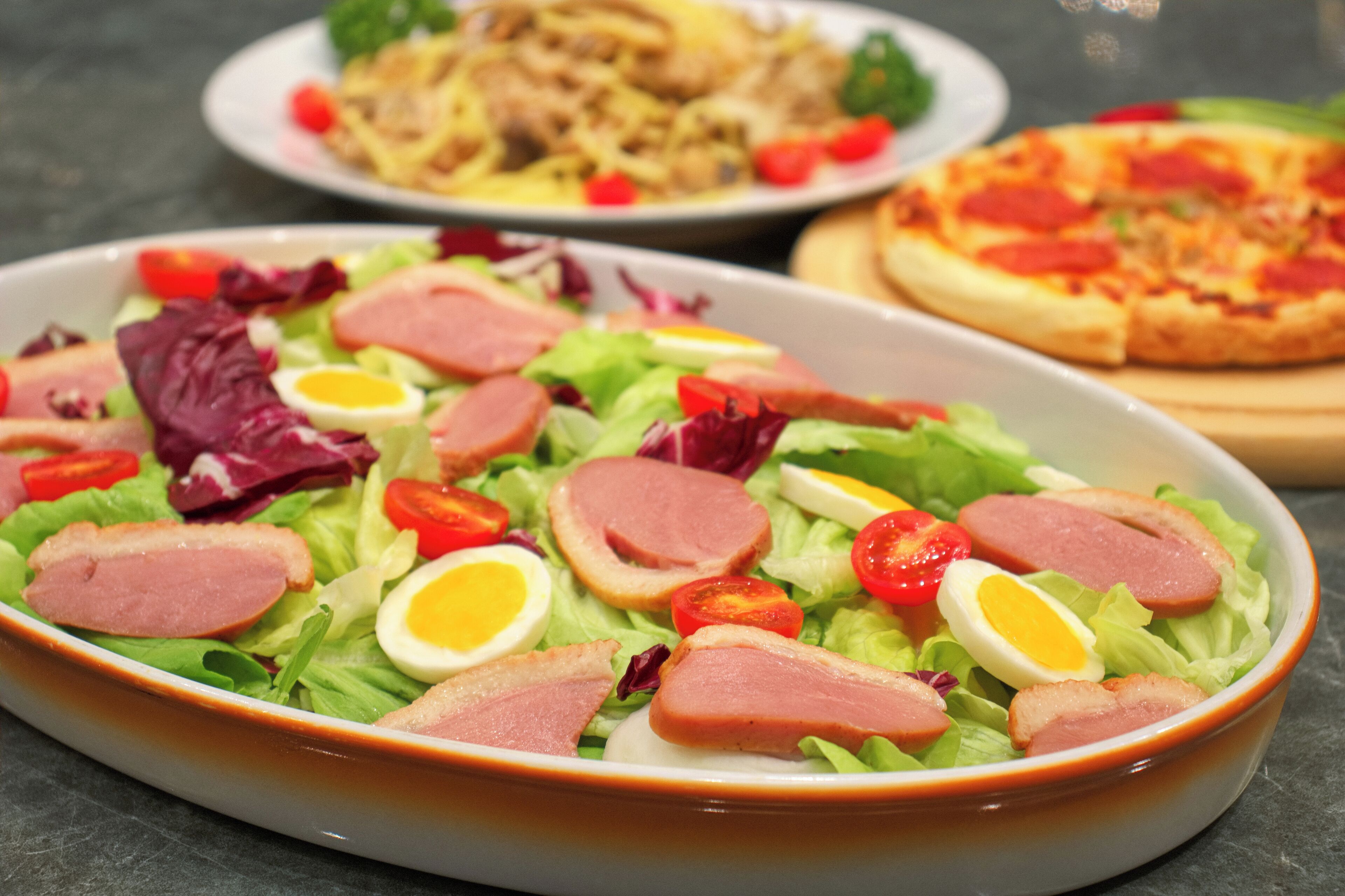 A salad with various ingredients, a plate of pasta, and a pizza.