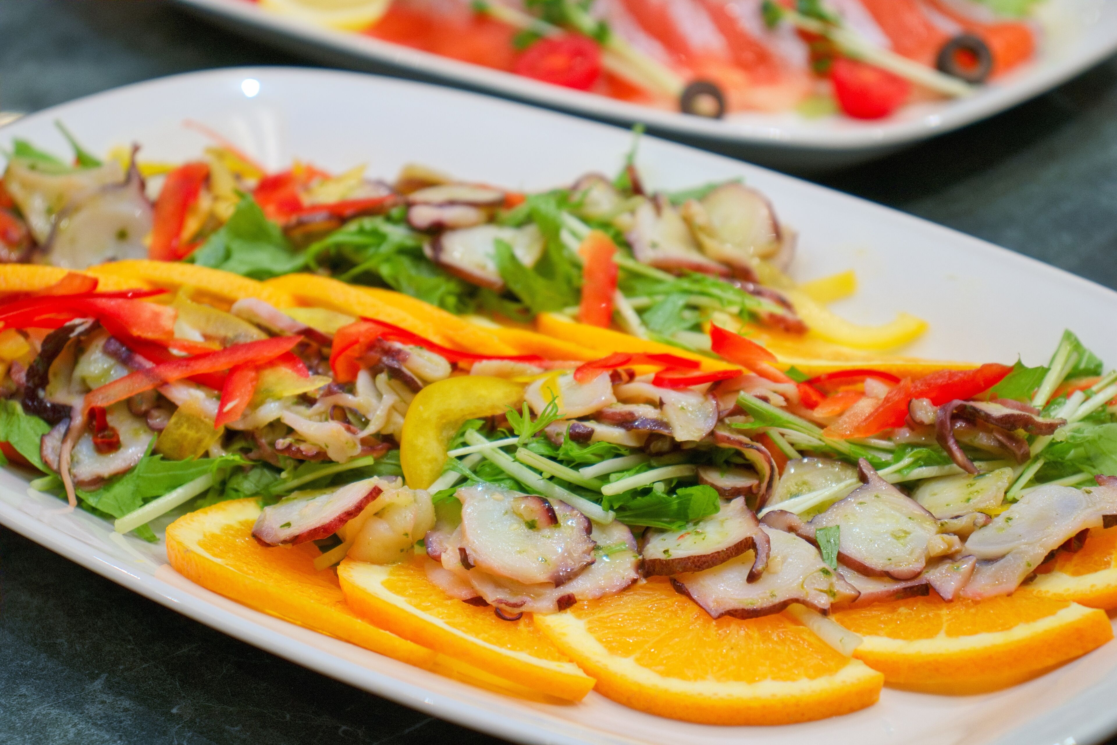 A plate of salad with various vegetables and slices of orange.