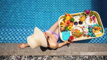 A person lying on a poolside lounge chair with a tray of food and drinks.