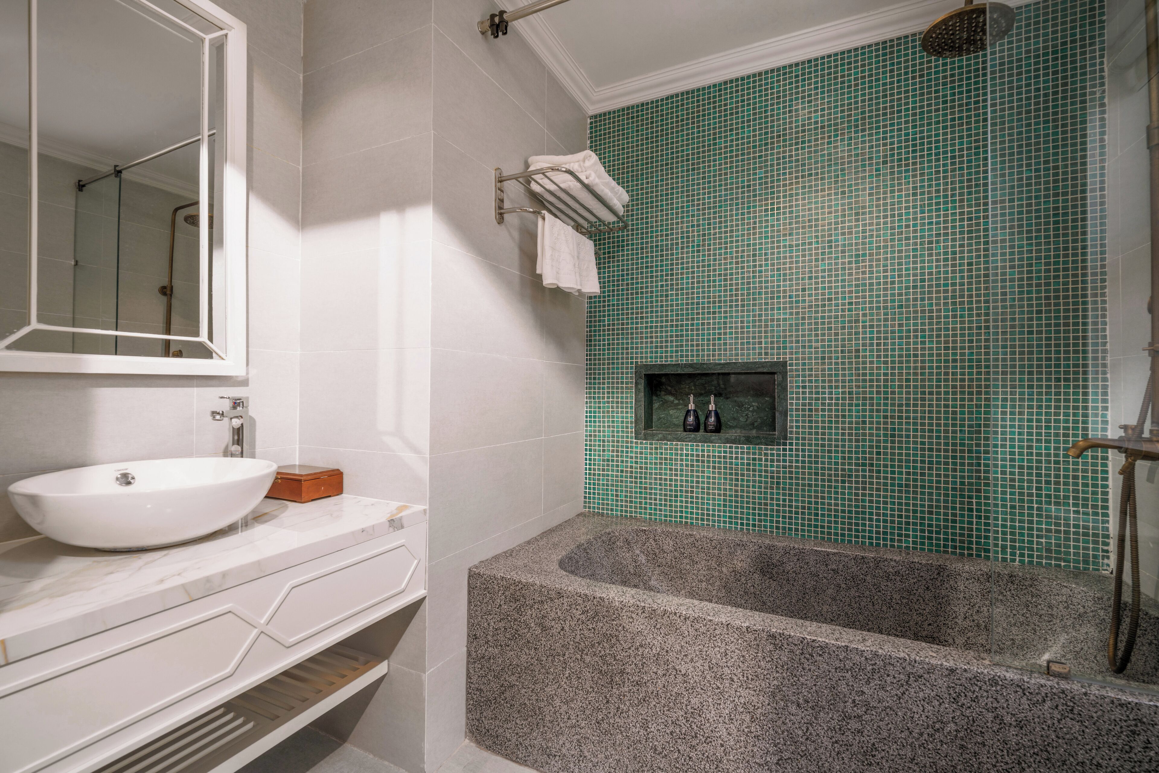A bathroom with a white sink, a marble vanity, a freestanding bathtub, and a green-tiled shower area.