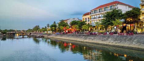 A riverside view with a bridge, buildings with balconies, and outdoor seating along the water.
