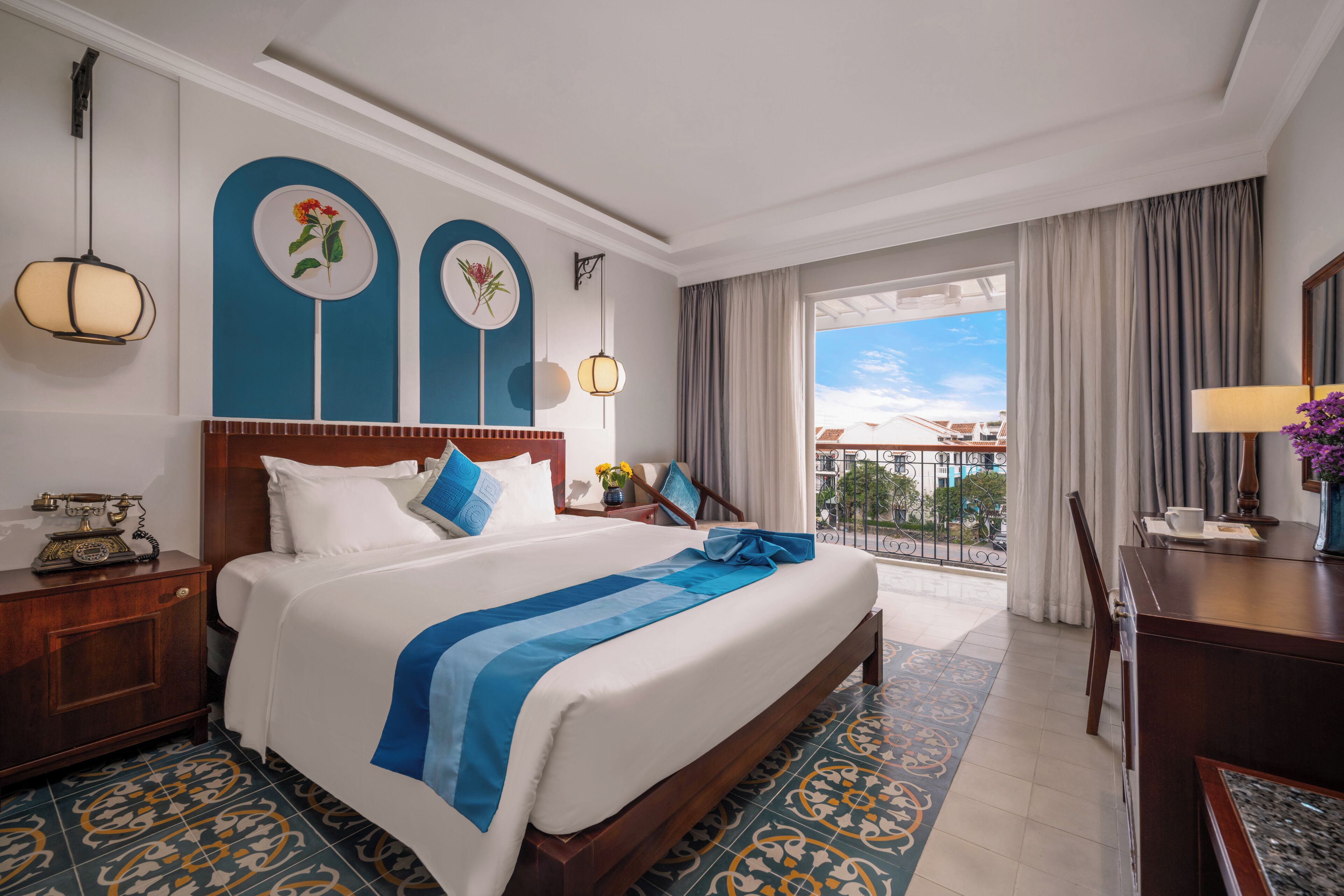 A hotel room with a large bed, a desk, a chair, a balcony with a view, and a decorative wall.