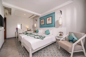 Una habitación de hotel con cama, escritorio, silla, televisor y lámpara fijada a la pared.