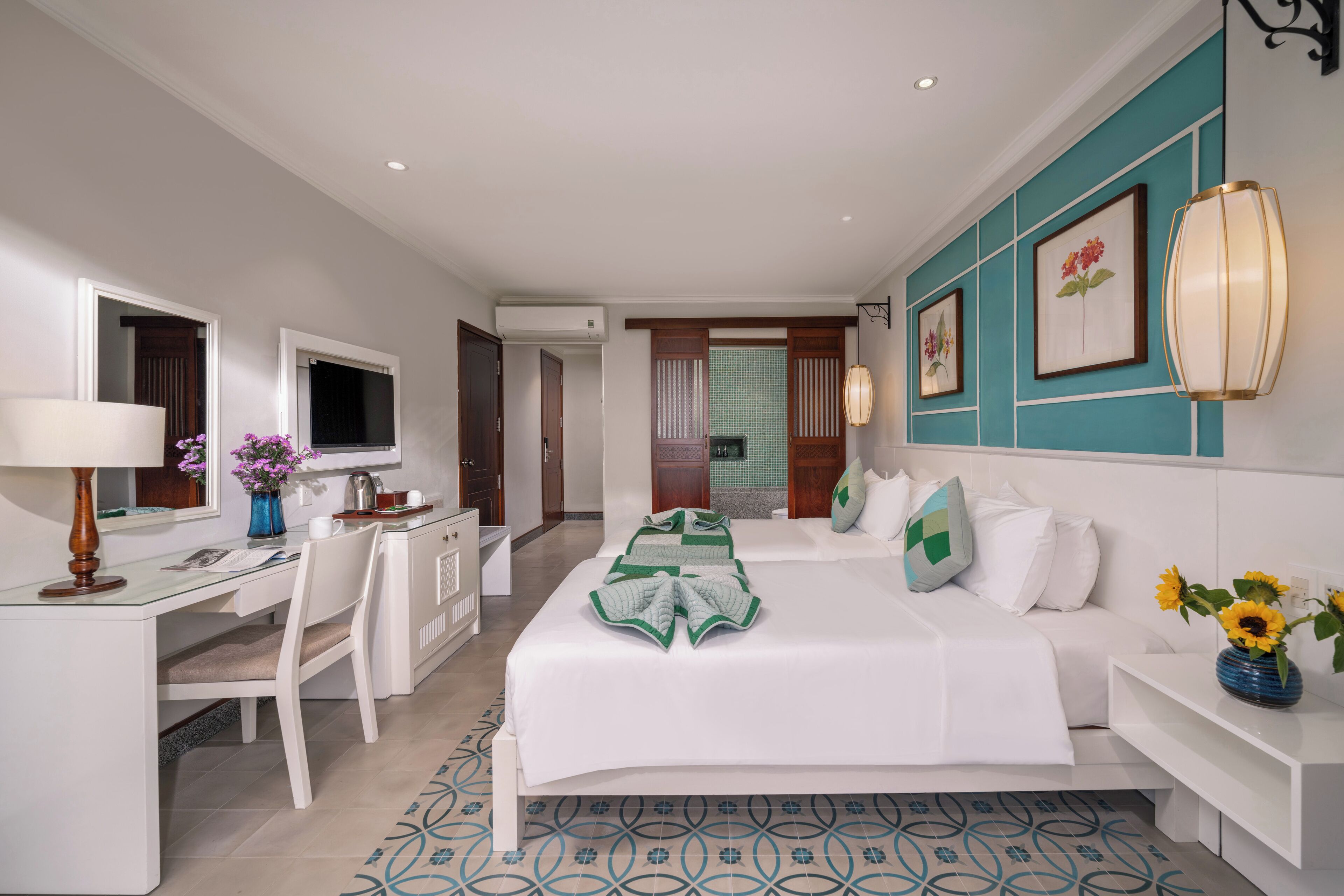 Quarto de hotel com cama, escrivaninha, cadeira e televisão.