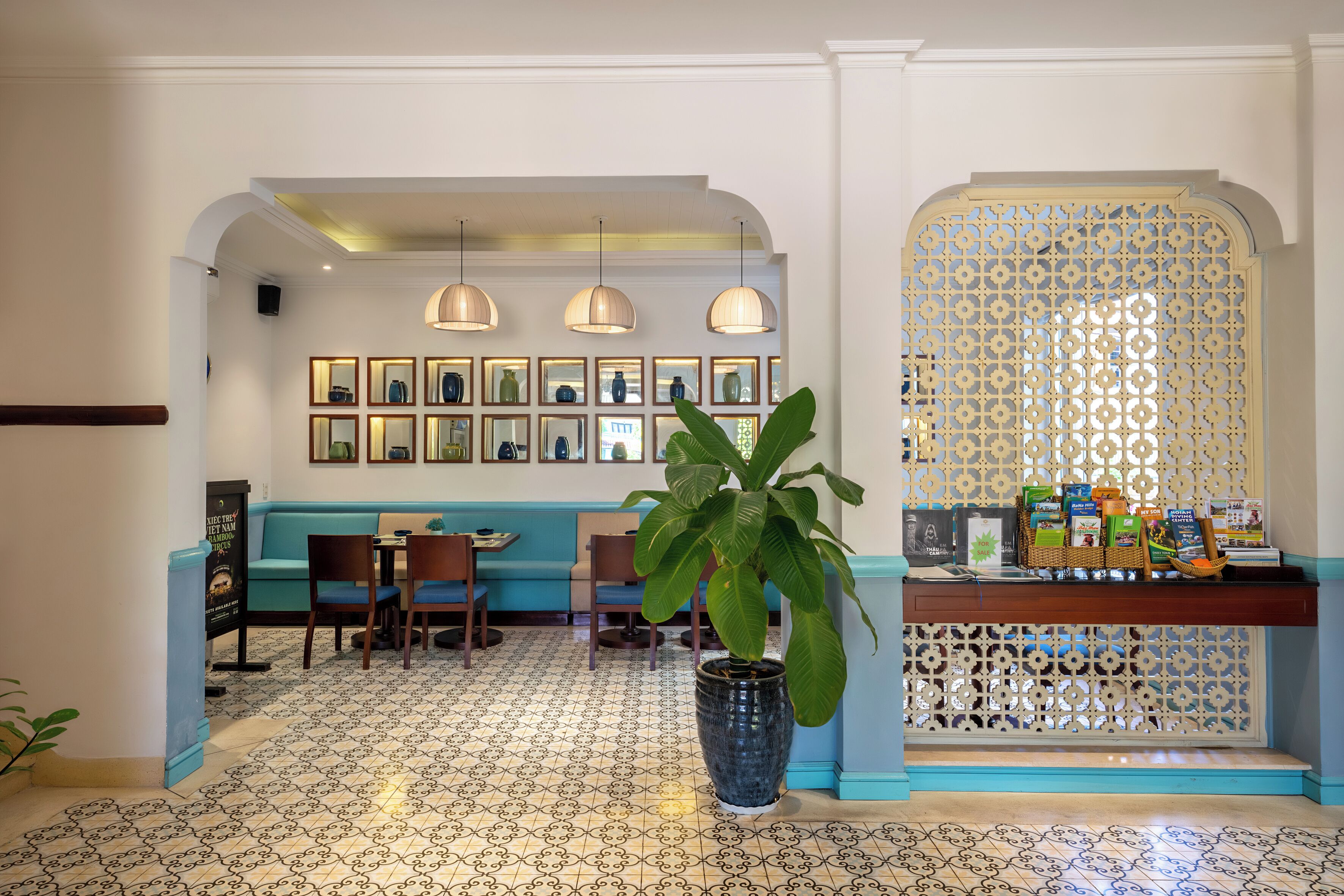 A restaurant with a blue and white tiled floor, a seating area with tables and chairs, a decorative plant, and a wall with framed pictures and a patterned screen.