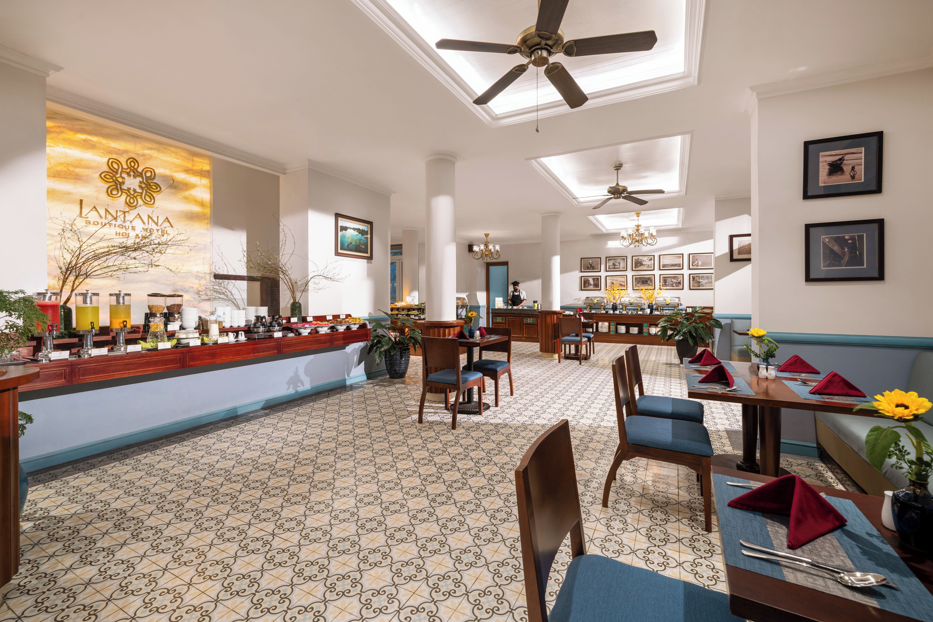 A hotel lobby with a bar area, dining tables with red napkins, and a patterned floor.