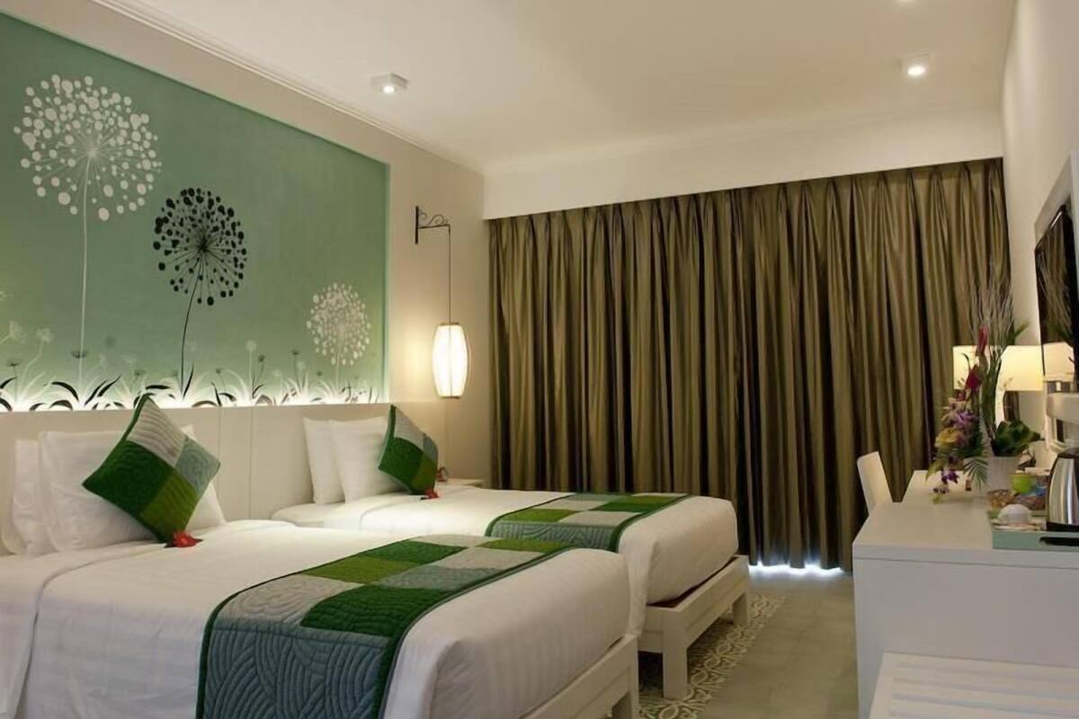 Habitación de hotel con dos camas, un cuadro verde en la pared, un ventanal con cortinas y un escritorio con lámpara.