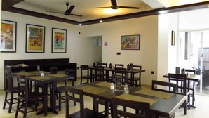 A spacious dining area with multiple tables and chairs, ceiling fans, and framed artwork on the walls. - Chapelton House (Colombo)