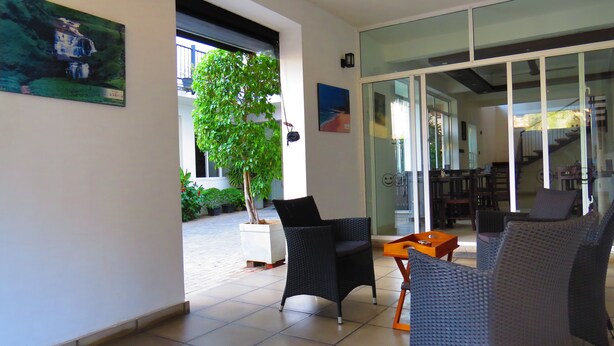 A modern interior with a glass door leading to a dining area, a potted tree, and a seating area with wicker furniture. - Chapelton House (Colombo)