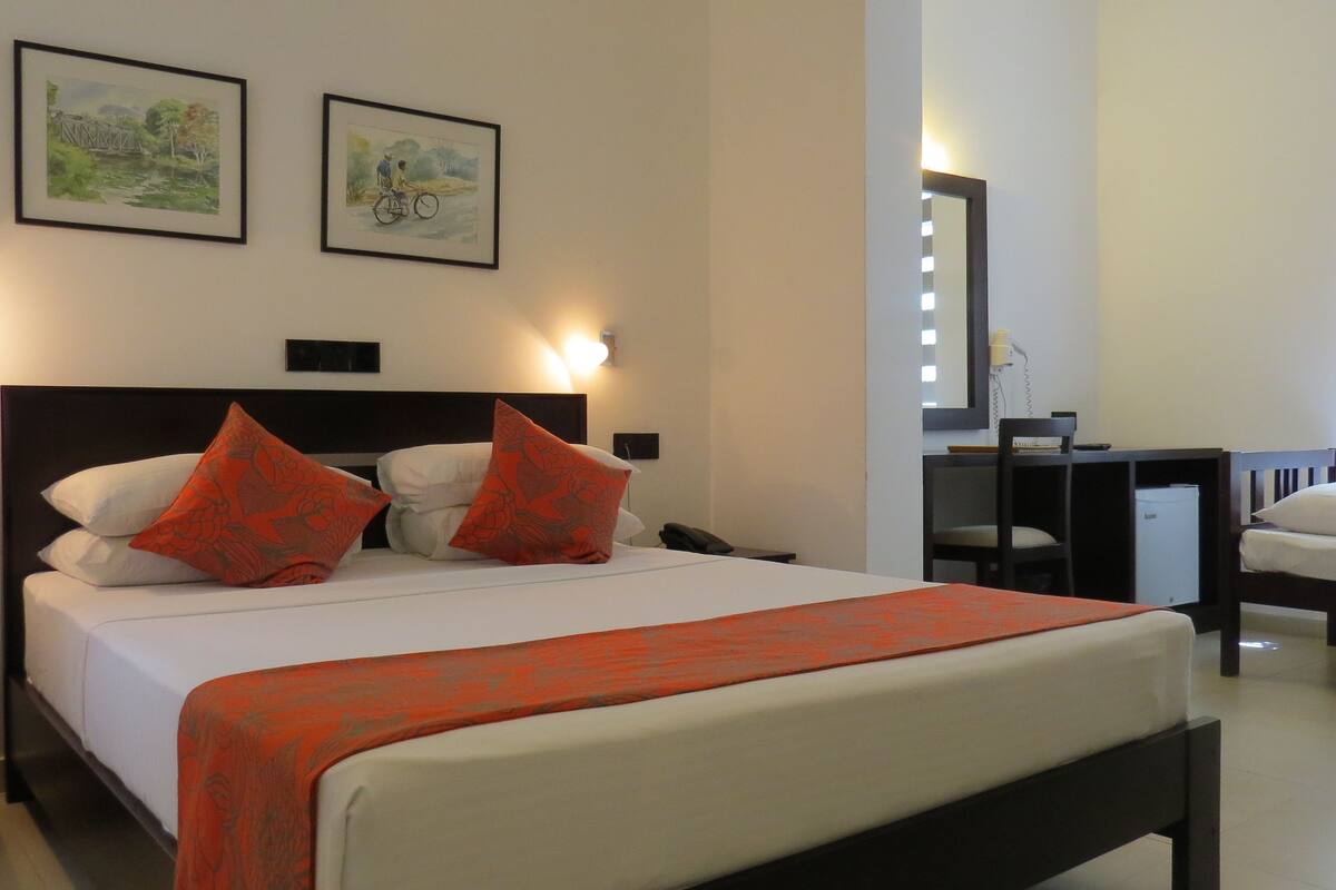 A hotel room with a bed, a desk, and a chair. There are two framed pictures on the wall.