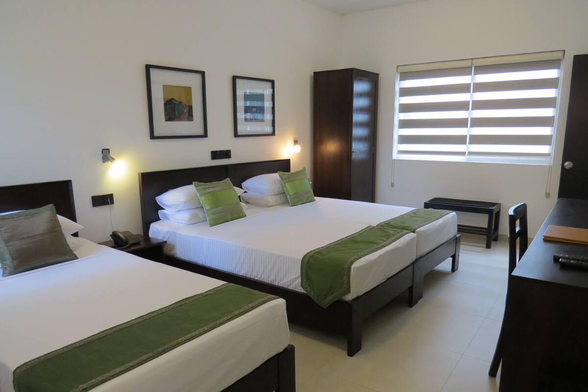 A hotel room with two single beds, a desk, a chair, and a window with blinds.