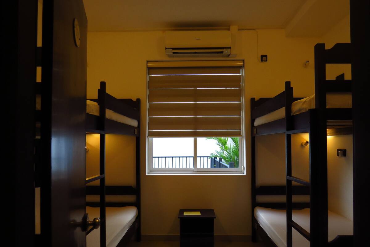 A room with bunk beds, a window with blinds, an air conditioning unit, and a small table with a note.