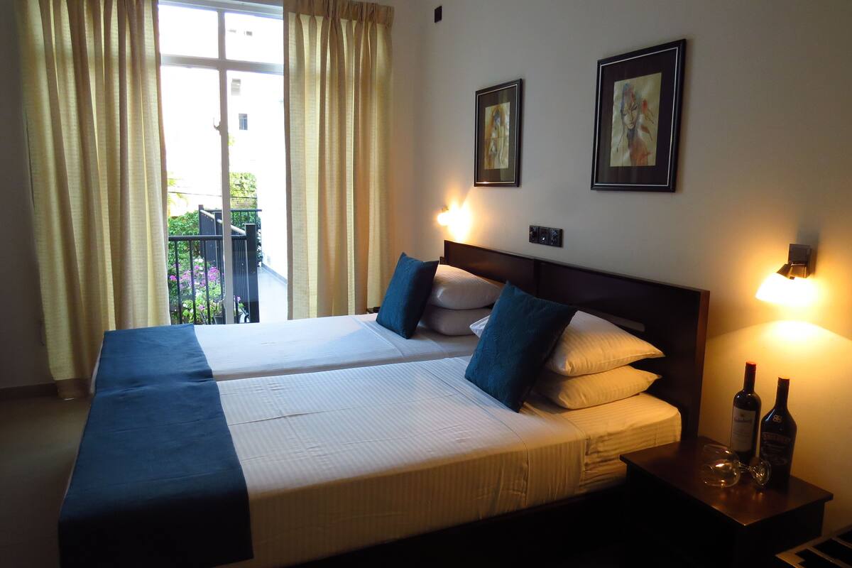 A double bed with a dark headboard, two pillows, and a bedside table with two bottles and glasses.