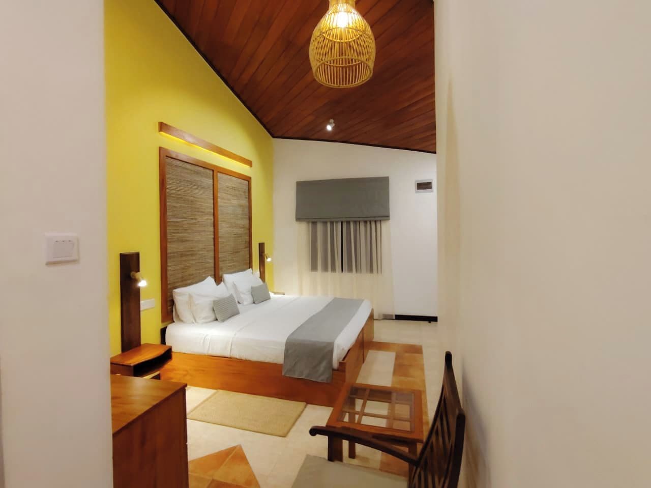 A bedroom with a bed, bedside tables, a wooden ceiling, and a hanging light fixture.