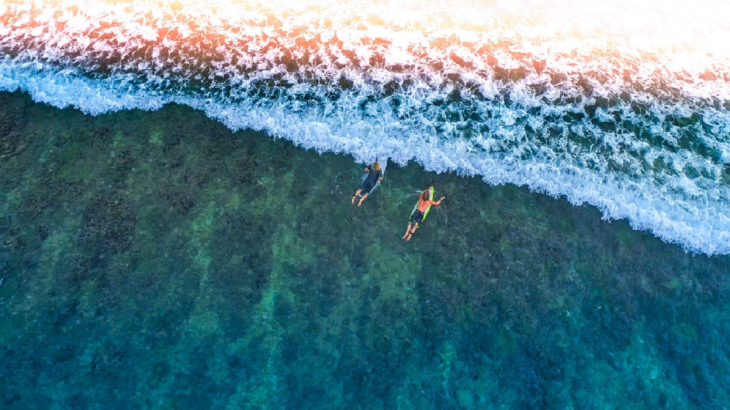 An aerial view of a beach with clear turquoise water and a foamy wave breaking at the shore.
