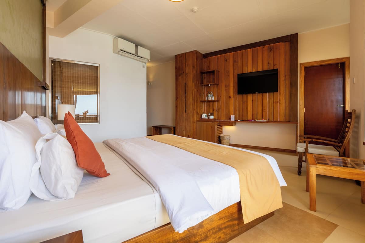 A hotel room with a large bed, wooden panel walls, a flat-screen TV mounted above a wooden shelf, and a wooden chair.
