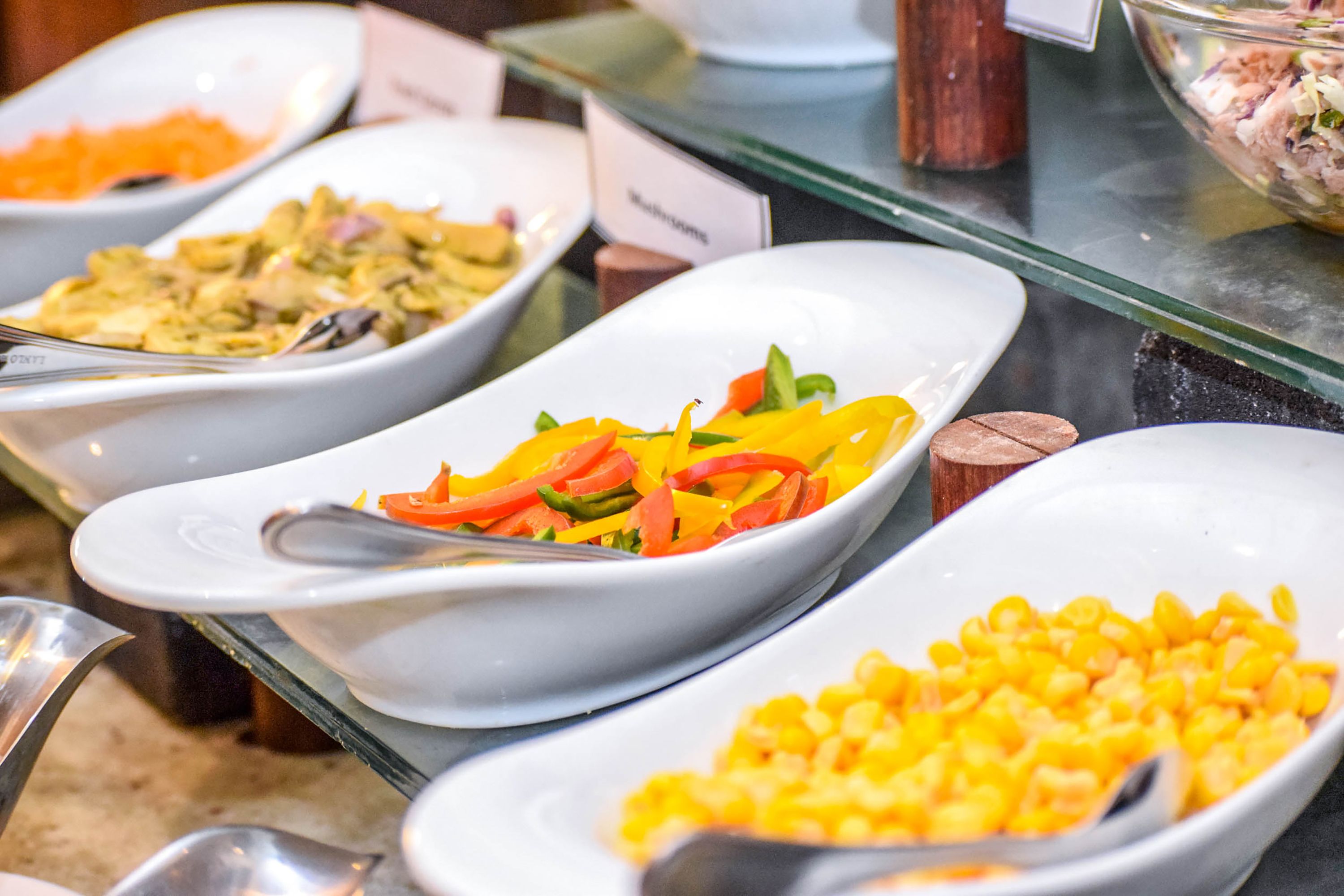 Ein Buffet mit verschiedenen Speisen, darunter ein Salat mit Paprika, ein Gericht mit Mais und ein Gericht mit der Aufschrift „Pilze“.