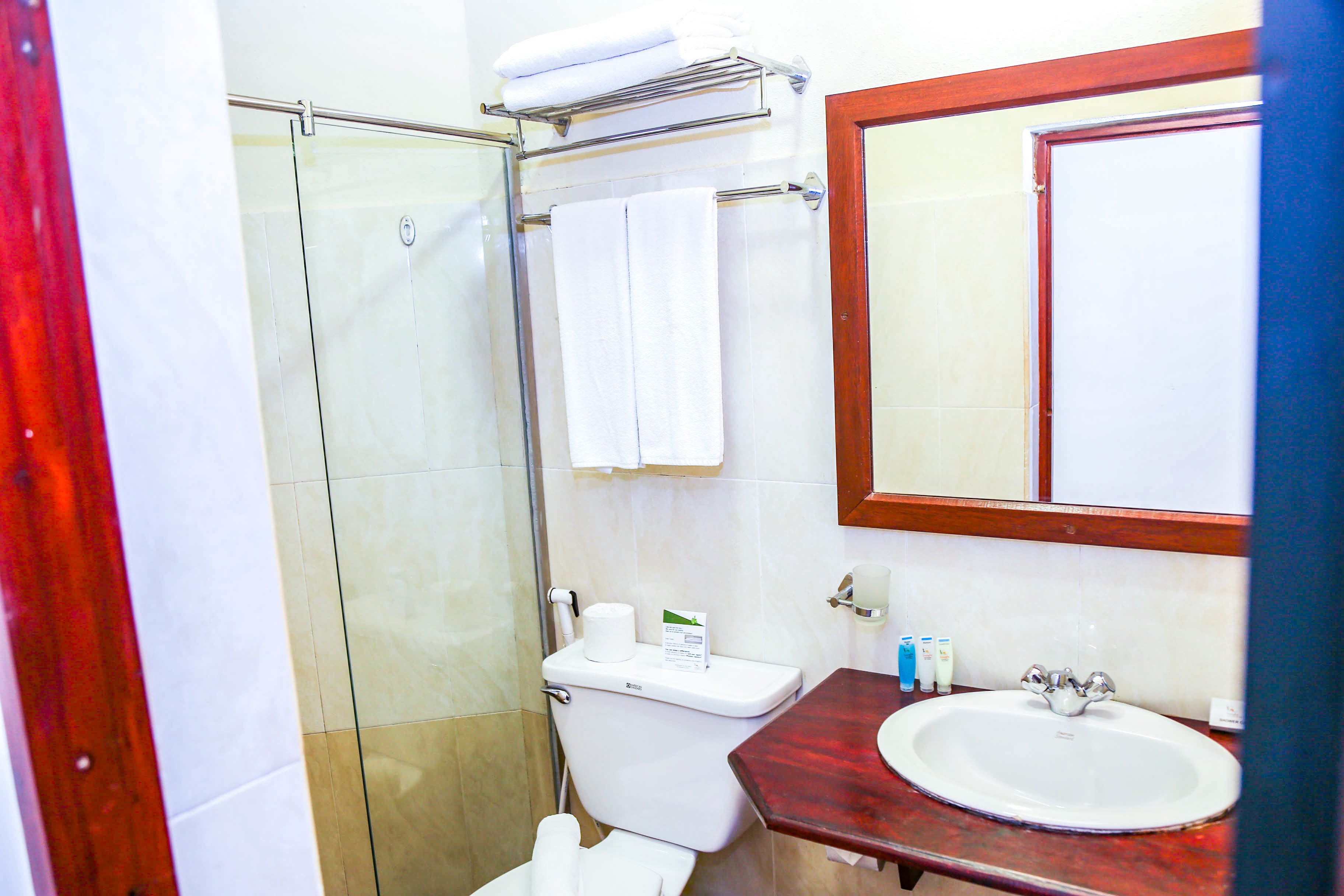 A bathroom with a glass shower enclosure, a toilet, a sink with a mirror above it, and a towel rack with towels.
