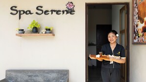 Entrada de un spa con un cartel que dice "Spa Serene", un estante de madera con plantas en macetas y una persona sosteniendo una bandeja con una bebida y una toalla.