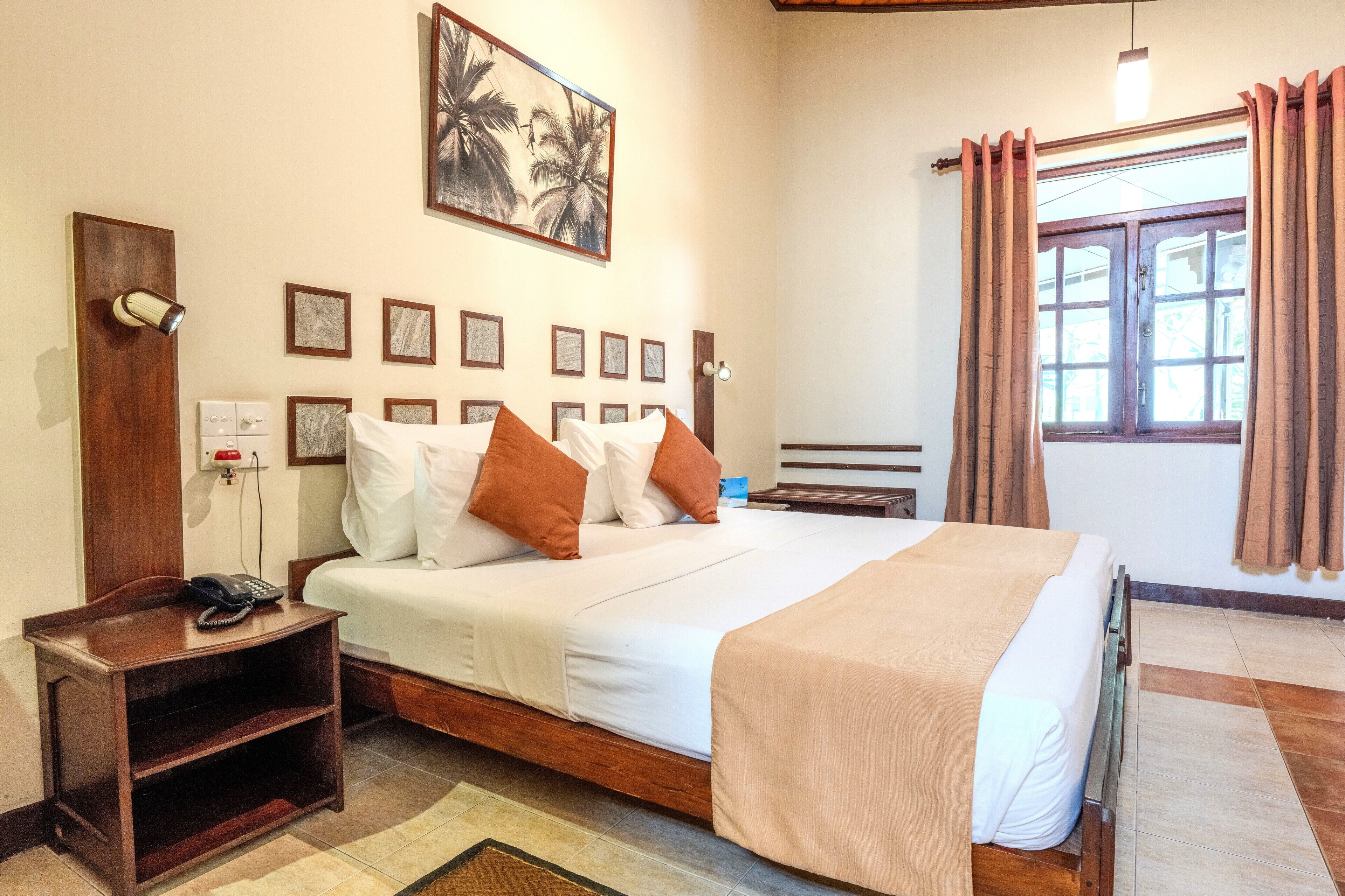 Habitación de hotel con cama, mesita de noche, lámpara, decoración en la pared y una ventana con cortinas.