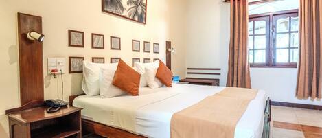 A hotel room with a bed, bedside table, lamp, wall art, and a window with curtains.