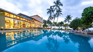 Un hotel con piscina, palmeras y un edificio con amplios ventanales.